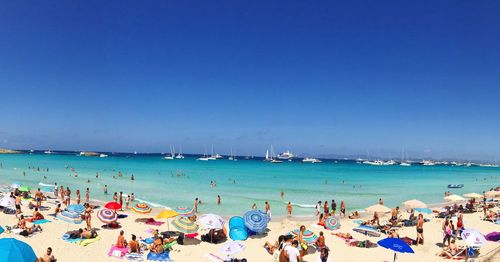 Panoramic view of people on beach against clear blue sky