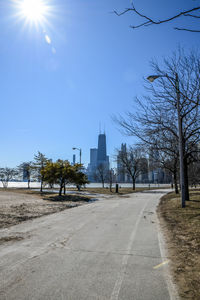 Road by trees and buildings against sky on sunny day