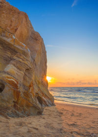 Rock formation on beach against sky during sunset