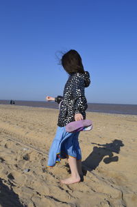 Full length of girl standing at beach against clear sky