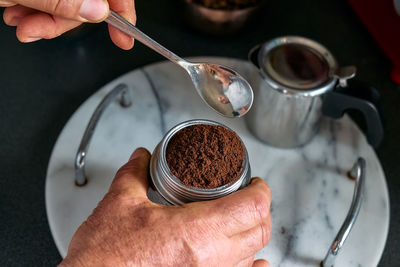 Man preparing classic italian coffee in the mocha, filling funnel of a moka pot with ground coffee.