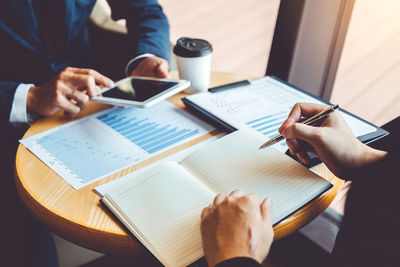 Midsection of colleagues with digital tablet and book analyzing charts in office