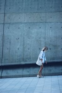 Full length of woman walking on footpath against wall