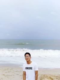 Portrait of young man standing at beach against sky