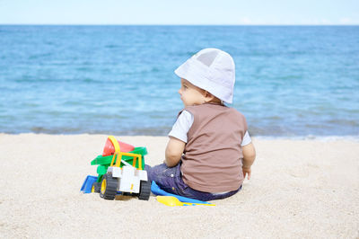 Rear view of baby boy sitting by toys at beach