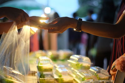 Cropped hands of customer taking money from vendor at market during dusk