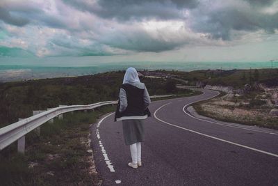Rear view of woman on road against cloudy sky