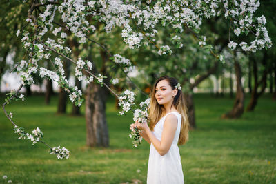 A young happy woman walks through an apple orchard among spring white flowers