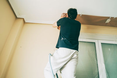 Rear view of man standing against wall at home