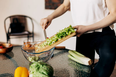 A woman cuts celery on a wooden board and transfers it to a transparent salad plate
