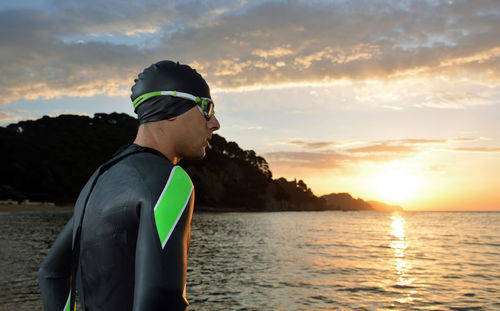 Man wearing wetsuit while standing at beach against orange sky