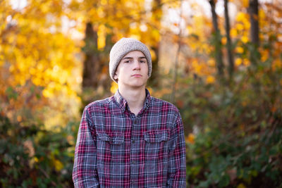 Serious teen boy in beanie and plaid shirt outdoors stares at camera