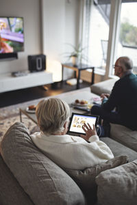 High angle view of senior woman using digital tablet while male partner sitting on sofa in living room