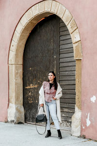 Full length portrait of stylish young woman in front of old door in city.