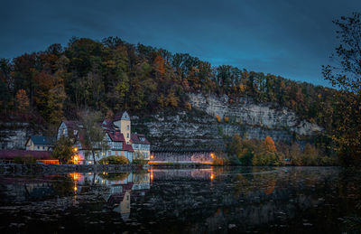 Lake by illuminated building against sky