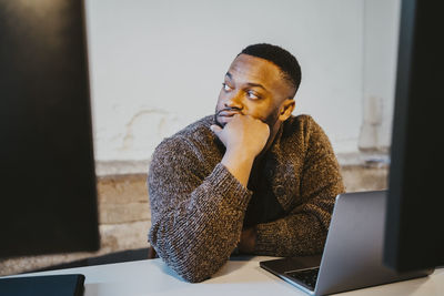 Contemplative male programmer looking away while sitting at desk in creative office