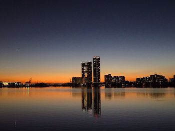 Reflection of illuminated buildings in calm sea against clear sky