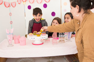 Woman putting cupcakes on tray by children during birthday party