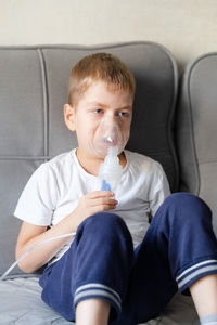 Portrait of young woman drinking water while sitting on sofa at home