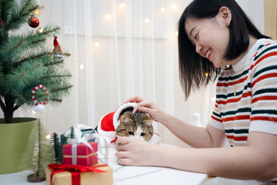 Asian woman decorate christmas tree and dressing her cat with christmas theme