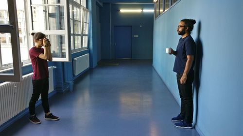 Side view of man photographing friend holding cup in corridor