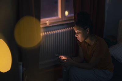 Young woman sitting on bed and using phone