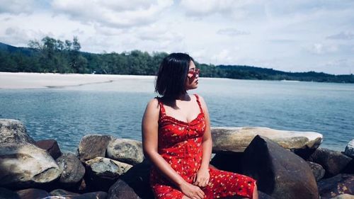 Woman sitting on rock looking at sea against sky
