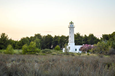 Lighthouse by trees on field against sky