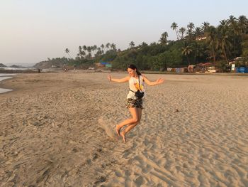 Playful young woman enjoying at beach against clear sky