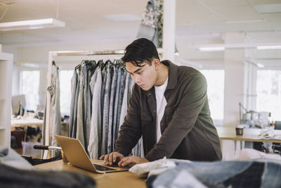 Concentrated male fashion designer using laptop at workshop