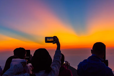 Rear view of people photographing at sunset