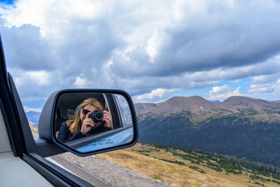 Reflection of woman photographing on side-view mirror of car