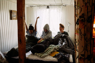 Male and female friends waking up on bed against window in cottage