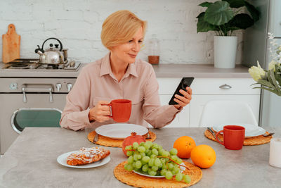 Woman holding mobile phone while sitting on table