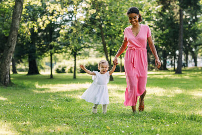 Full length of happy woman with arms raised on grass against trees