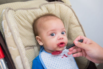 Cropped woman feeding baby boy on baby carriage at home