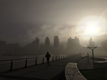 Silhouette man standing on sea by city against sky