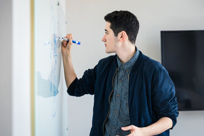 Young entrepreneur writing on whiteboard during meeting in board room