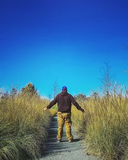 Rear view of man standing on field against clear blue sky