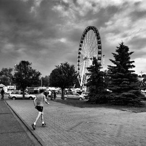 Rear view of man with ferris wheel against cloudy sky