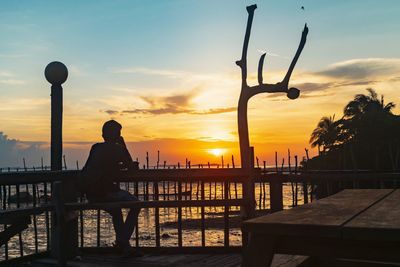 Silhouette man sitting on pier against sky during sunset