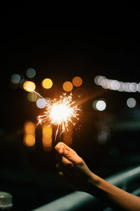 Hand holding illuminated firework display at night