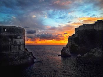 Sea by buildings against sky during sunset