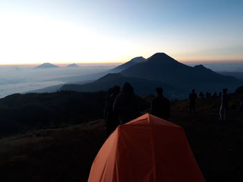 Tent behind silhouette people standing on mountain during sunrise