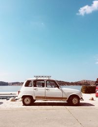Cars on road by sea against blue sky