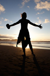 Side view of silhouette woman standing at beach against sky during sunset