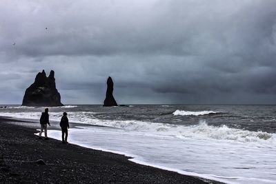 Male friends on shore against cloudy sky at vik