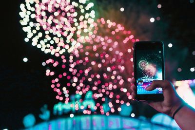 Midsection of person photographing illuminated mobile phone at night