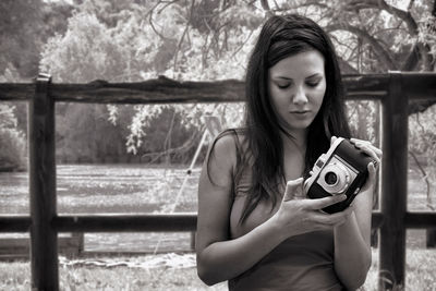 Young woman holding camera while standing at public park