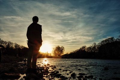 Silhouette man standing at lakeshore against sky during sunset